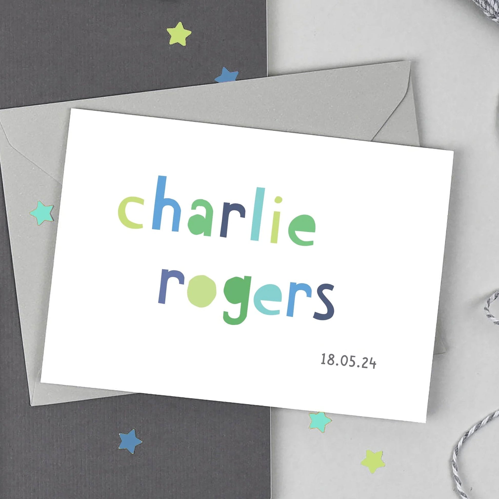 a personalised baby boy card by studio 9 ltd. the card has the childs first name and surname printed on the front in a cut out style blue and green font. Underneath the name is the childs date of birth.